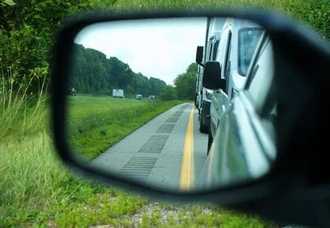 Car side mirror view of sleeper lines or rumble strips on road shoulders are  Stock Photos