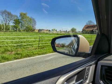 Car side view mirror reflects a serene rural landscape with green fields and Foto stock