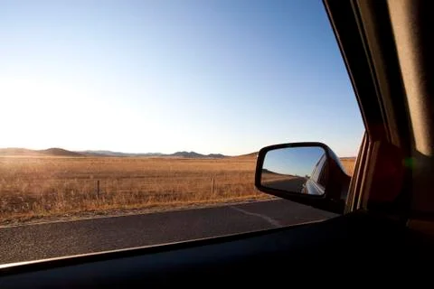 Car sideview mirror with road going through field in the background Stock Photos