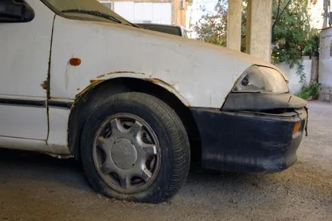 The car on the street is an old rusty with a flat tire and a broken headlight Stock Photos