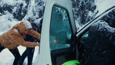 Car stuck in the snow on the road, man and his friends trying to get him out. Stock Footage 124526169