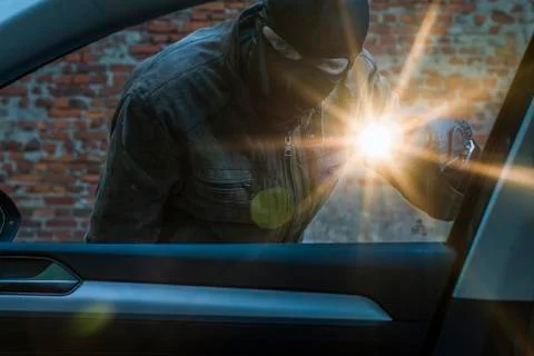 Car thief examines a car with a flashlight Stock Photos