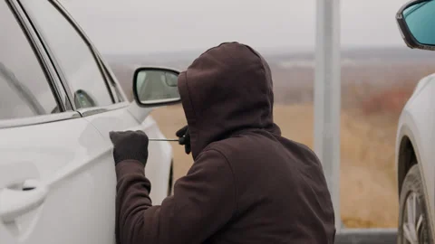 A car thief forcefully picks the lock of a white car using a screwdriver in this Stock Footage 267075255