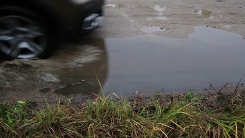 Car tire driving through large muddy puddle on rural dirt road, splashing water, Stock Footage 325699105