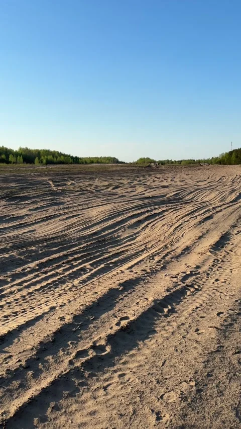 Car tire tracks on an open sandy field under a clear blue sky Stock Footage 334628814