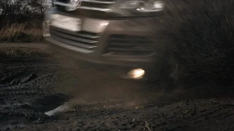Car tyre driving over deep puddle and splashing water across the dirt road. Видео 131739733