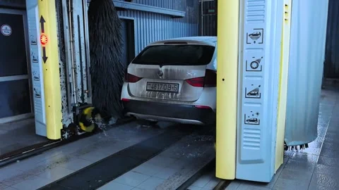 Car wash process in an automatic facility with brushes and water sprays on a wee Stock Footage 332133920