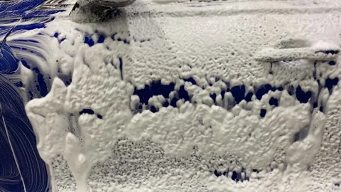 Car wash soap creating cascade of suds over blue car door Stock Footage 285234924