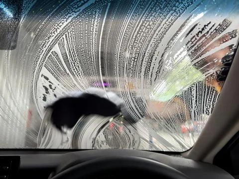 Car wash worker cleaning windshield by hand, sponge and foam bubbles Stock Photos