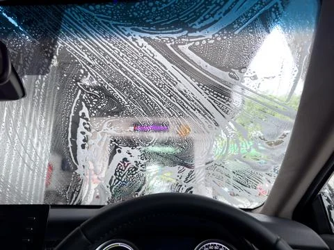 Car wash worker cleaning windshield by hand before washing machine tunnel Stock Photos