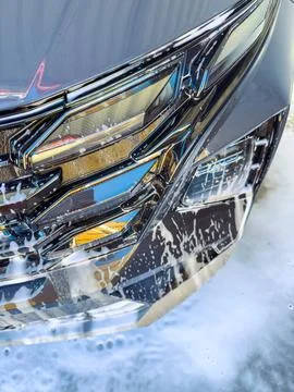 Car washing process shows close-up of car front with soap and water on surfac Stock Photos