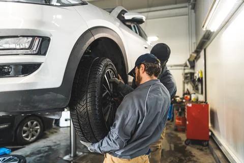 Car wheel changing process in the garage, two mechanics working in the workshop Stock Photos