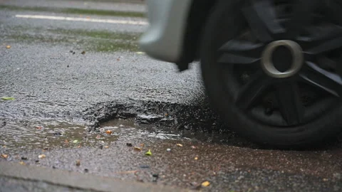 Car wheel driving through pothole, raining, road damage, UK, slomo. Potholes 스톡 동영상 237238664