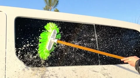 Car window being cleaned with brush and water under bright sunlight, Stock Footage 334102979