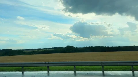 Car window view of a field with distant forest. Blue sky, clouds, and sun r.. Stock Footage 340546348