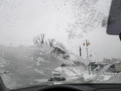 A car windshield covered with ice and snow blurs the view outside. The scene Stock Photos