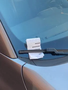 Car windshield with a folded parking ticket tucked under the wiper, symboli.. Stock Photos