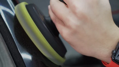 In car workshop, worker applies polish to black car body using a special roller. Stock Footage 115931695