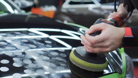 In car workshop, worker applies polish to black car body using a special roller. Stock Footage 115934675