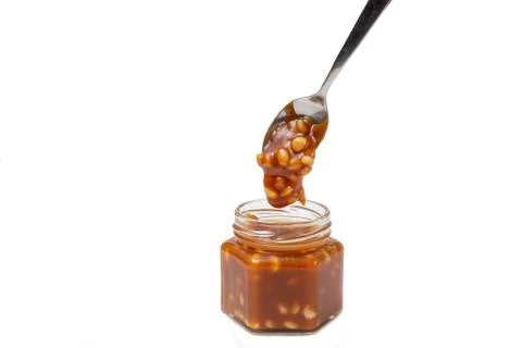 Caramel flows down from a spoon into a jar on a white background Stock Photos