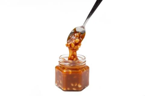 Caramel flows down from a spoon into a jar on a white background Stock Photos