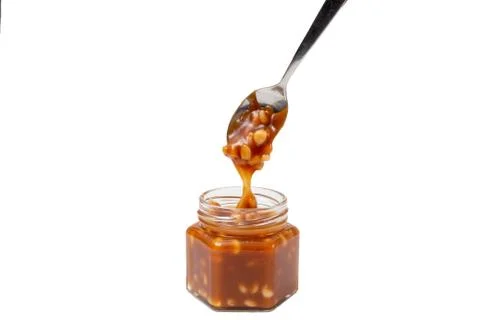 Caramel flows down from a spoon into a jar on a white background Stock Photos