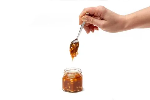 Caramel flows down from a spoon into a jar on a white background Stock Photos