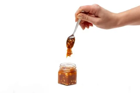 Caramel flows down from a spoon into a jar on a white background Stock Photos