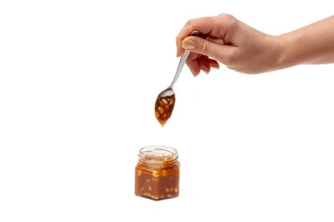 Caramel flows down from a spoon into a jar on a white background Stock Photos