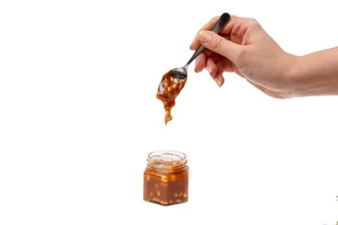 Caramel flows down from a spoon into a jar on a white background Stock Photos