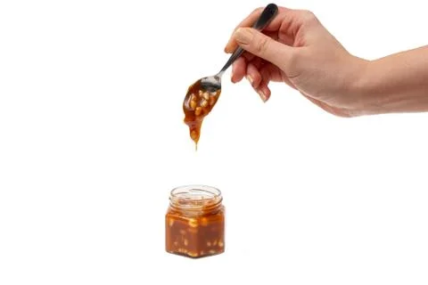 Caramel flows down from a spoon into a jar on a white background Stock Photos