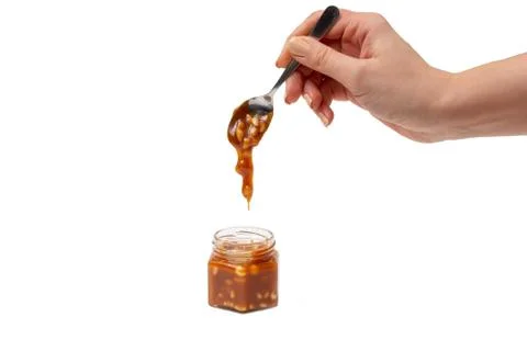 Caramel flows down from a spoon into a jar on a white background Stock Photos