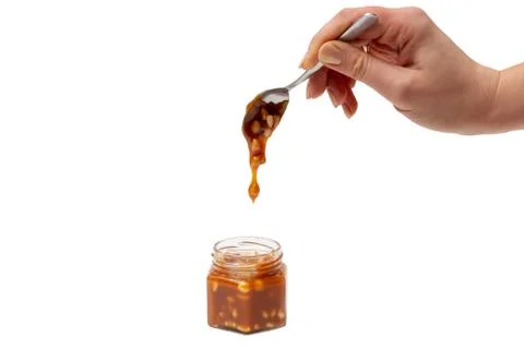 Caramel flows down from a spoon into a jar on a white background Stock Photos