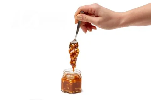 Caramel flows down from a spoon into a jar on a white background Stock Photos