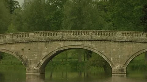 Caravan crossing old stone bridge spanning still river on gloomy day. Stock Footage 10579909