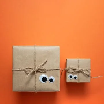 Card with brown craft gift boxes with eyes on orange background. Stock Photos