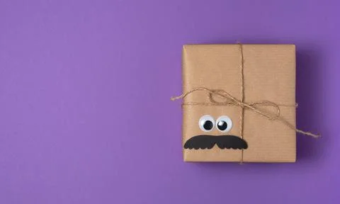 Card with brown craft gift boxes with eyes and mustache on lilac background. Stock Photos