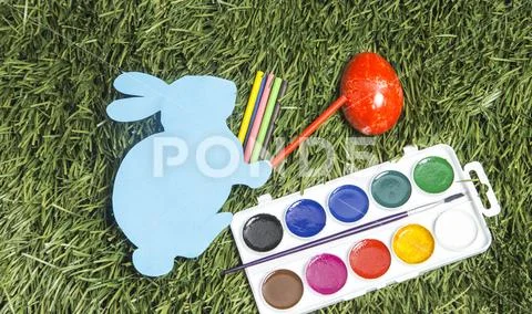 Card bunny with colorful markers on it's hand, painting egg into red. Stock Photos