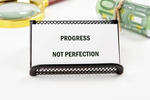 A card displays the message PROGRESS NOT PERFECTION. Nearby, a rolled bundle of Stock Photos