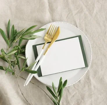 Card mockup on table place setting with cutlery, olive branch on neutral beige c Stock Photos