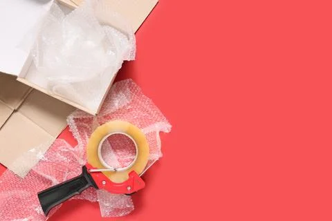 Cardboard box with bubble wrap and packing tape dispenser on red background f Stock Photos