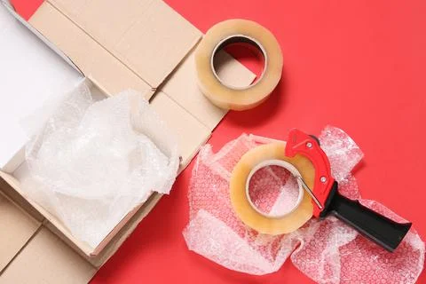 Cardboard box with bubble wrap, packing tape, and dispenser on red background Stock Photos