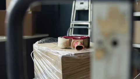 Cardboard Box Wrapped in Plastic with Tape Dispenser in Warehouse Stock Footage 337305056