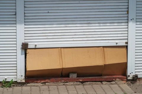 Cardboard boxes blocking partially opened metal shop shutter entrance Stock Photos