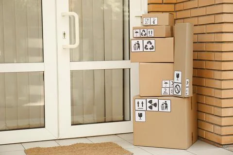 Cardboard boxes with different packaging symbols on porch near entrance, spac Stock Photos