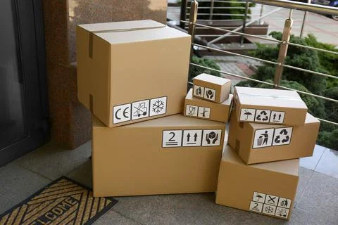 Cardboard boxes with different packaging symbols on porch near entrance. Parc Stock Photos