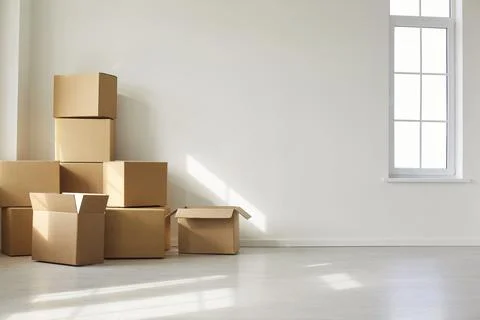 Cardboard Boxes Stacked in Bright Empty Room Near Window Stock Photos