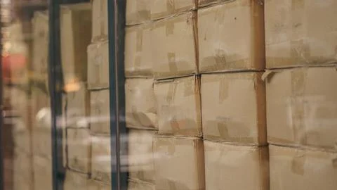 Cardboard boxes stacked inside distribution warehouse behind glass window clo Stock Photos
