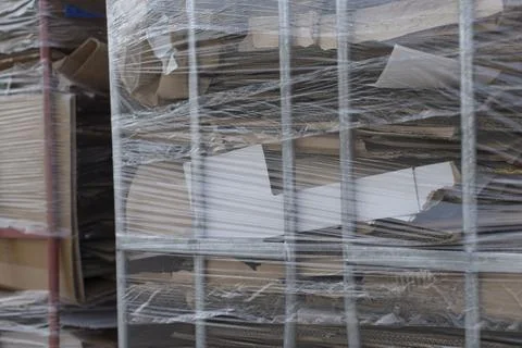 Cardboard boxes wrapped in plastic are behind a metal fence Stock Photos