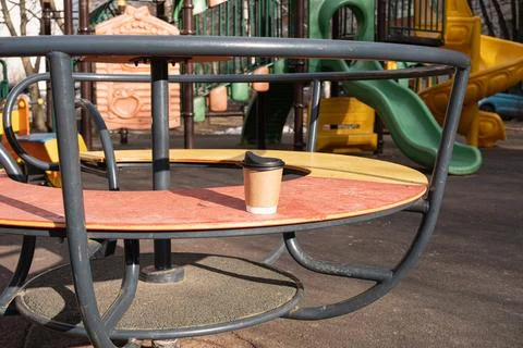 Cardboard coffee cup rests on circular metal playground carousel Stock Photos